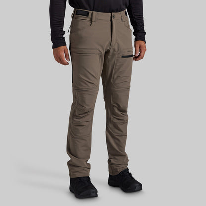 A man modeling grey technical cargo pants against a solid gray background.