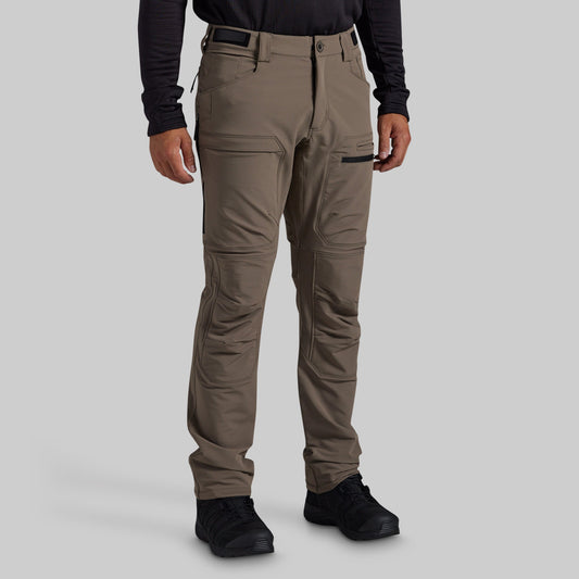 A man modeling grey technical cargo pants against a solid gray background.
