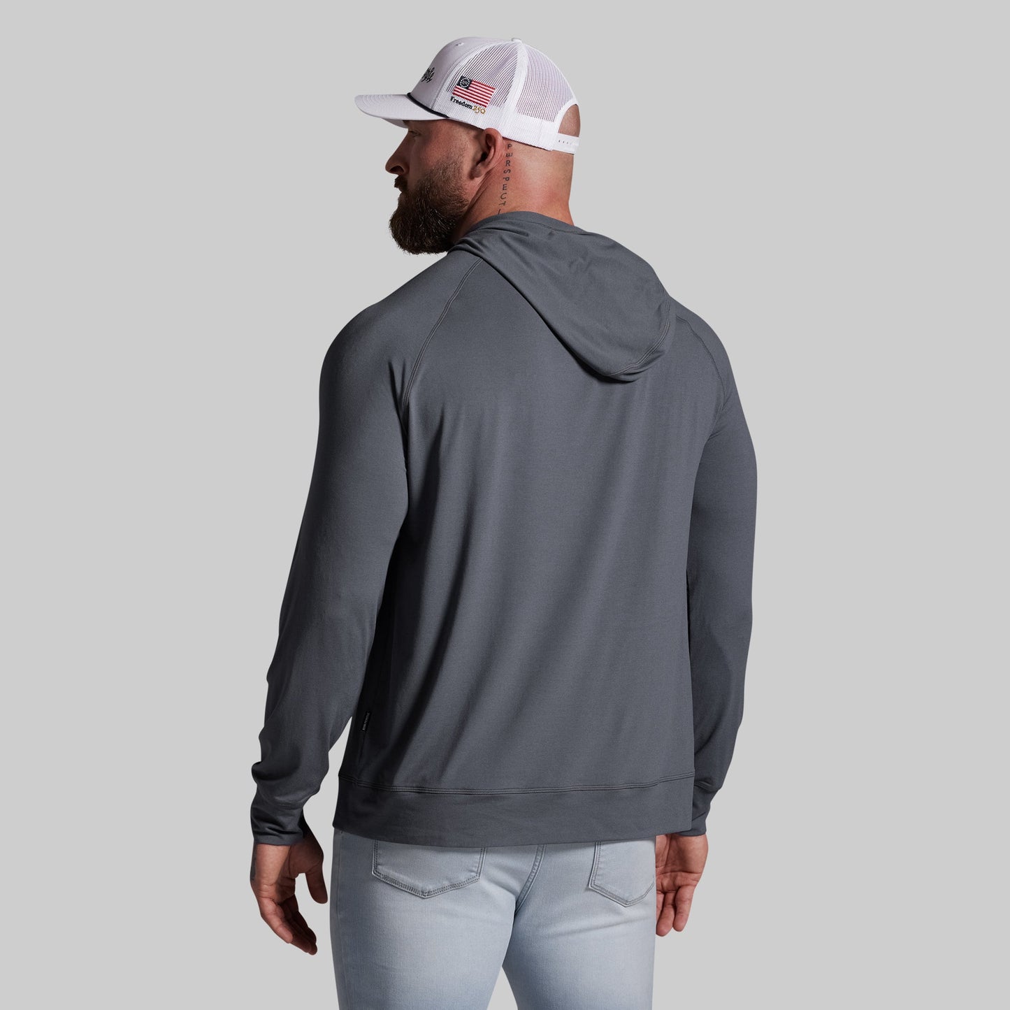 Man wearing a gray hoodie and light blue jeans on a gray background