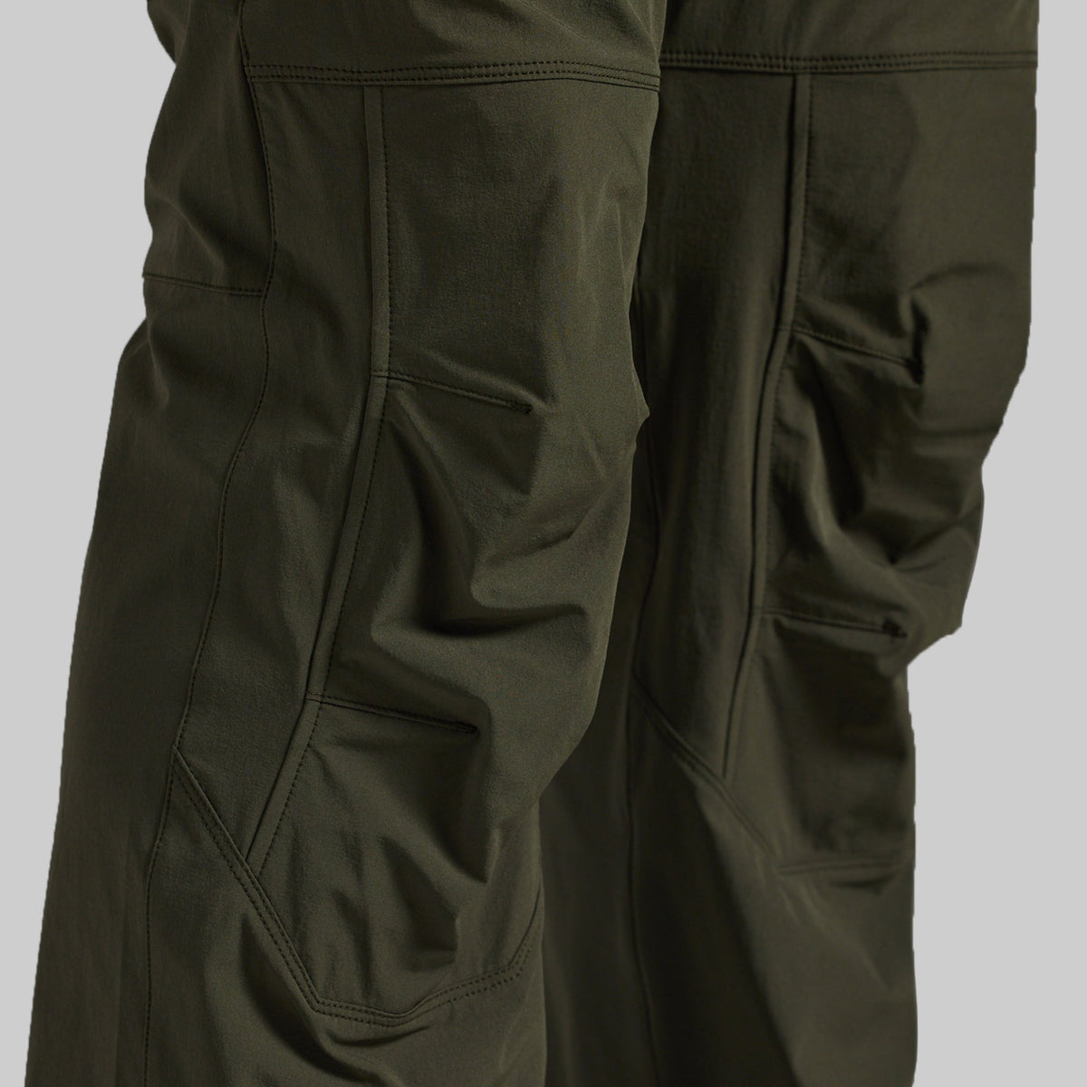 Close-up of dark olive green outdoor pants showing the fabric texture, seams, and side pockets against a neutral gray background.