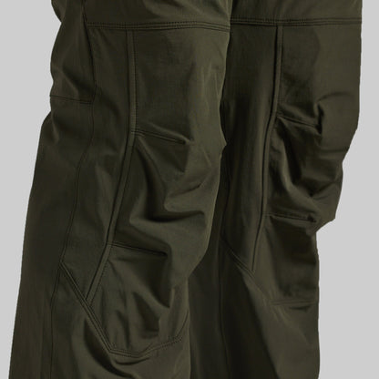 Close-up of dark olive green outdoor pants showing the fabric texture, seams, and side pockets against a neutral gray background.