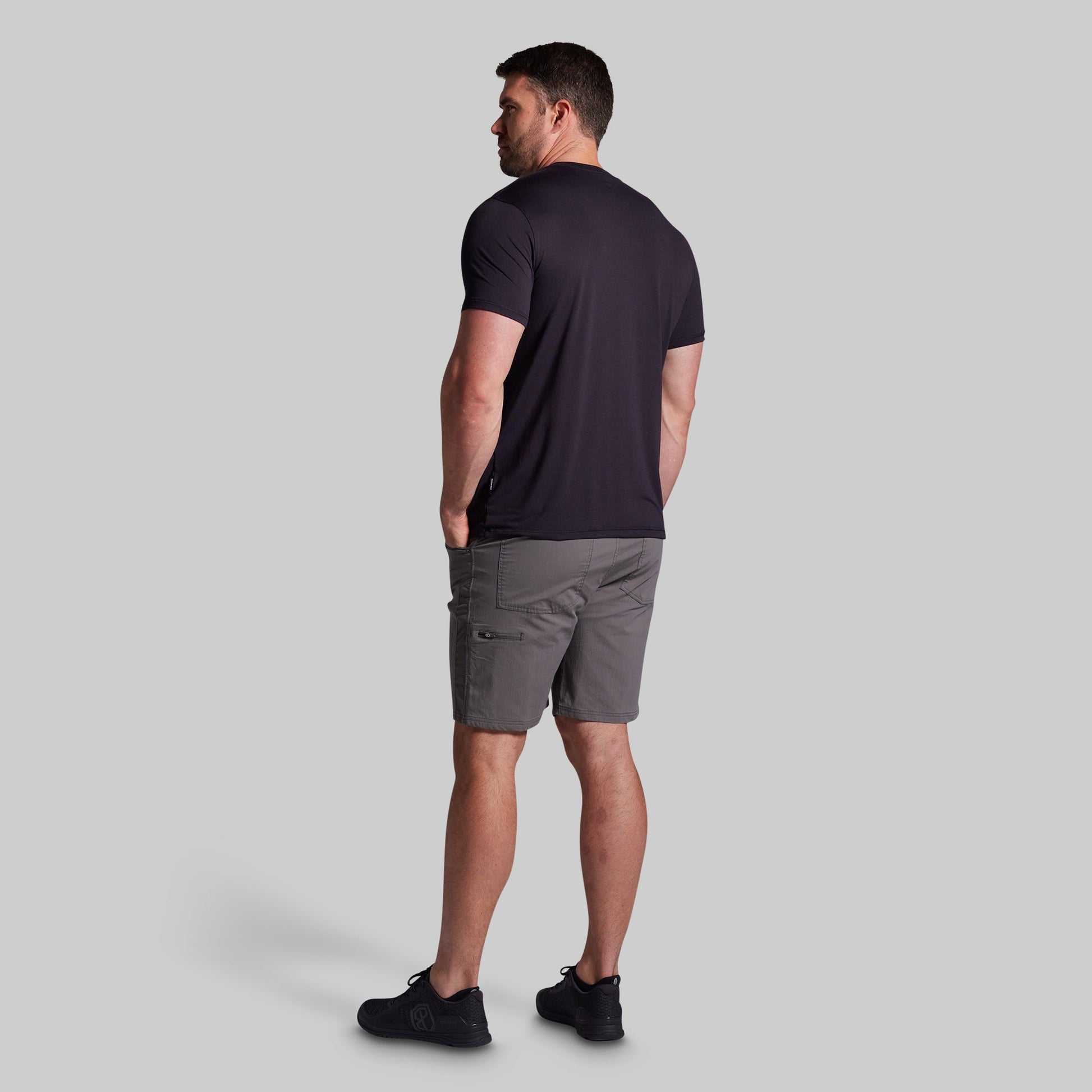 Man wearing a black t-shirt and gray shorts on a light gray background