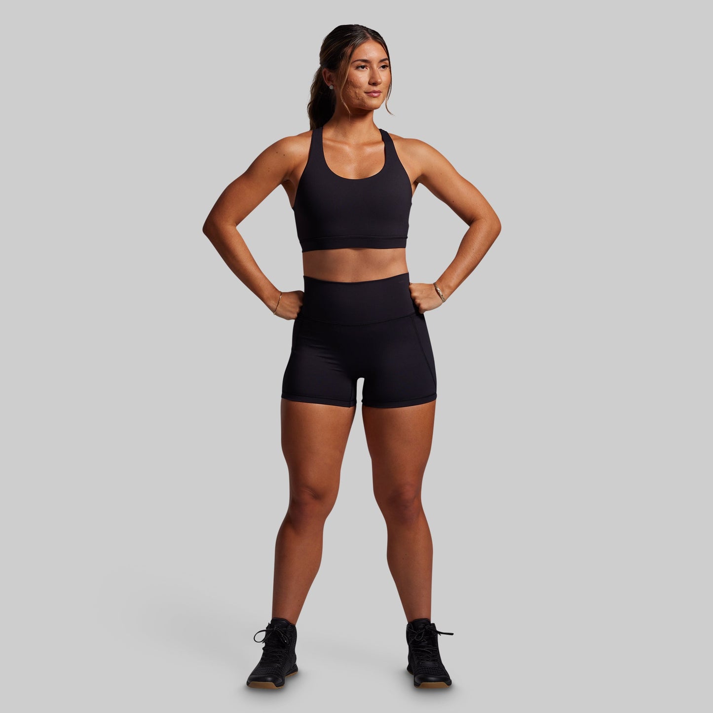 Woman wearing a black sports bra and shorts on a gray background