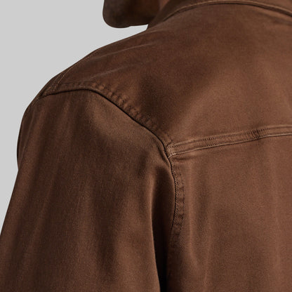 Close-up of a brown textured jacket or overshirt showing the shoulder seam, collar, and fabric texture against a light gray background.