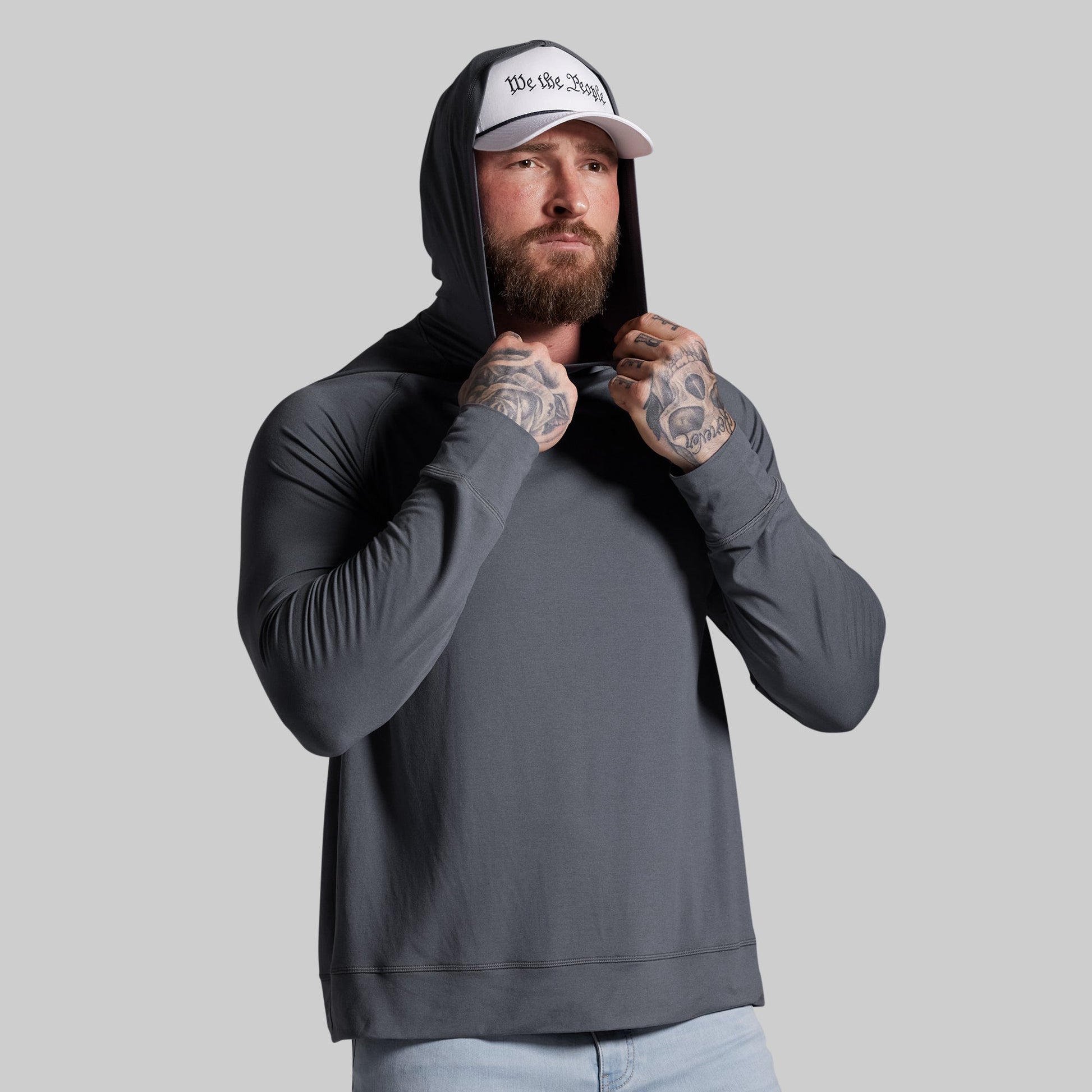 Man wearing a gray hoodie and white cap with text, standing against a plain background