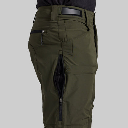 Close-up of olive green cargo pants with multiple zippered pockets, shown on a model from the waist down against a light gray background.
