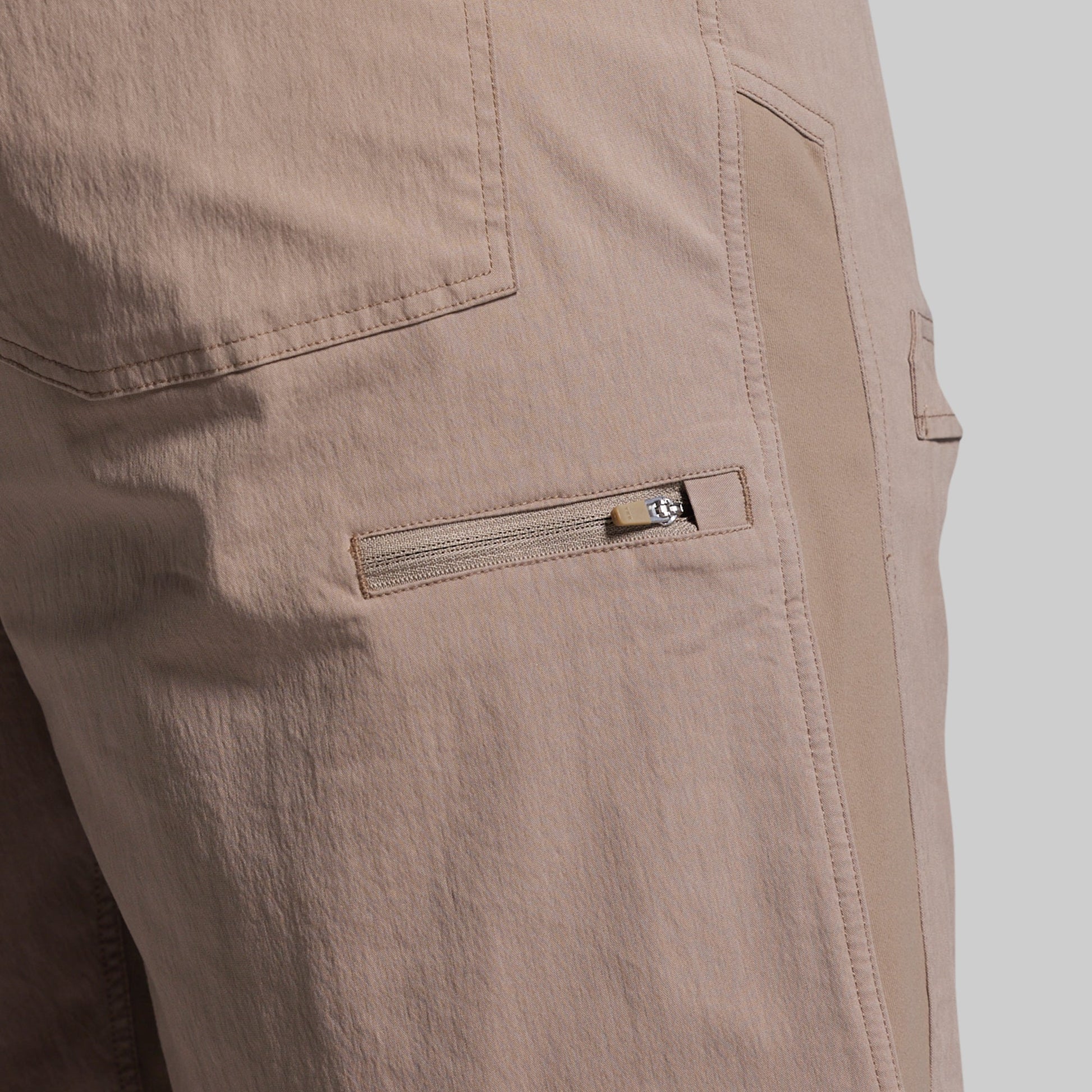 Close-up of beige shorts with a zipper pocket on a light gray background
