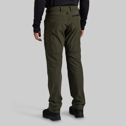 A person shown from the back wearing olive green technical cargo pants, a black long-sleeve top, and black shoes against a light gray studio background.