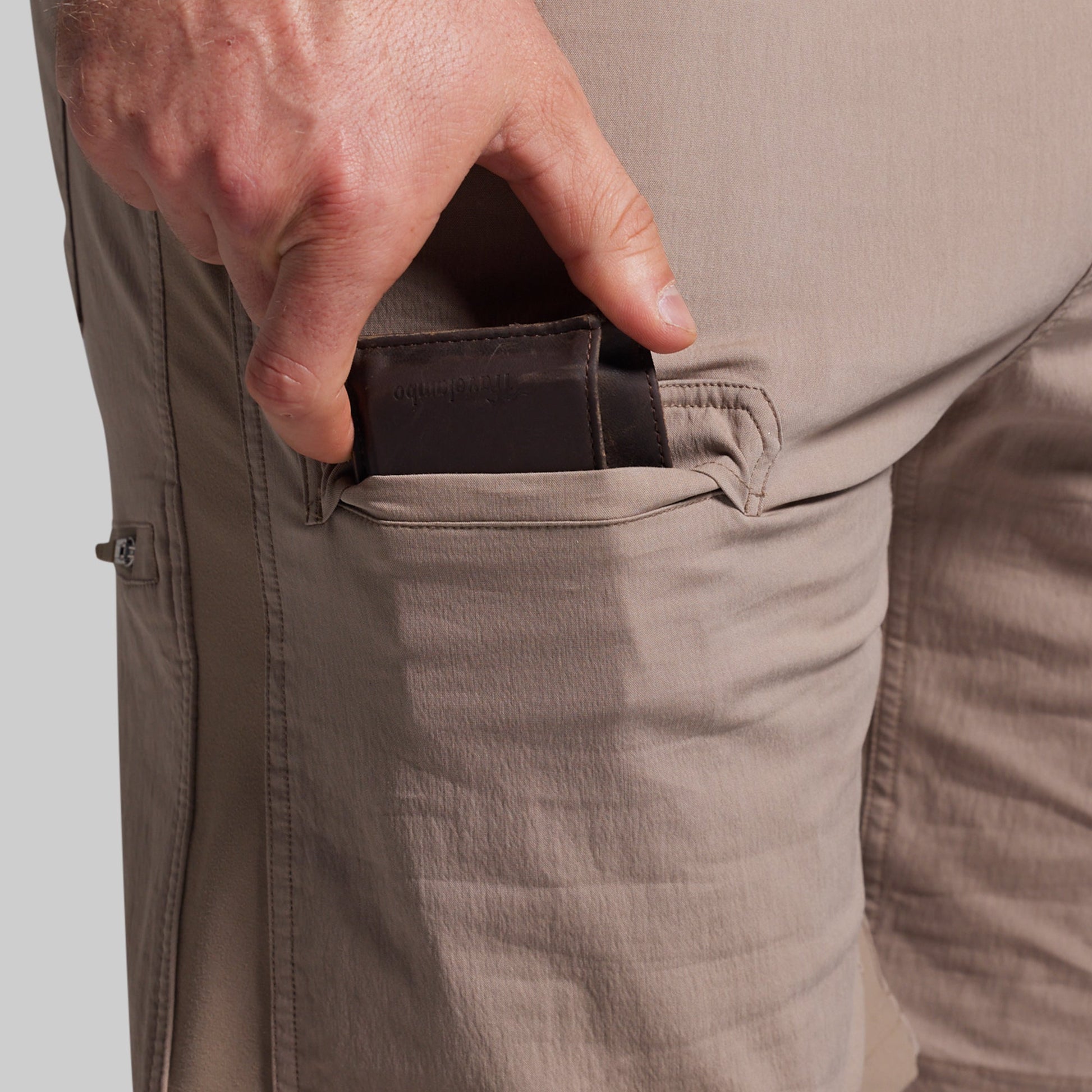 Person wearing beige shorts with a hand reaching into a pocket on a light gray background