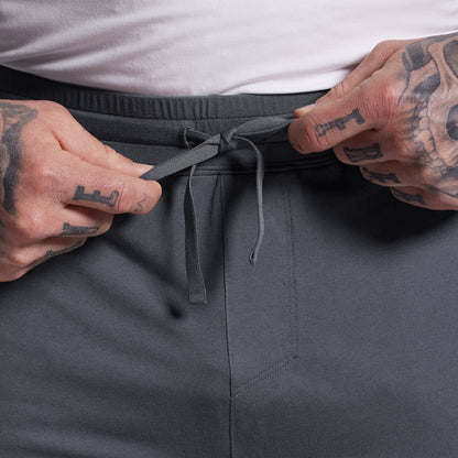 Person adjusting the drawstring of gray shorts with a tattooed hand.