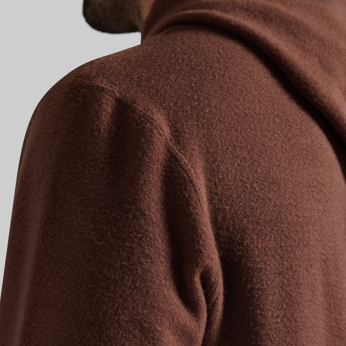 Close-up of a person wearing a brown textured hooded sweatshirt, showing the shoulder and neck area against a light gray background.