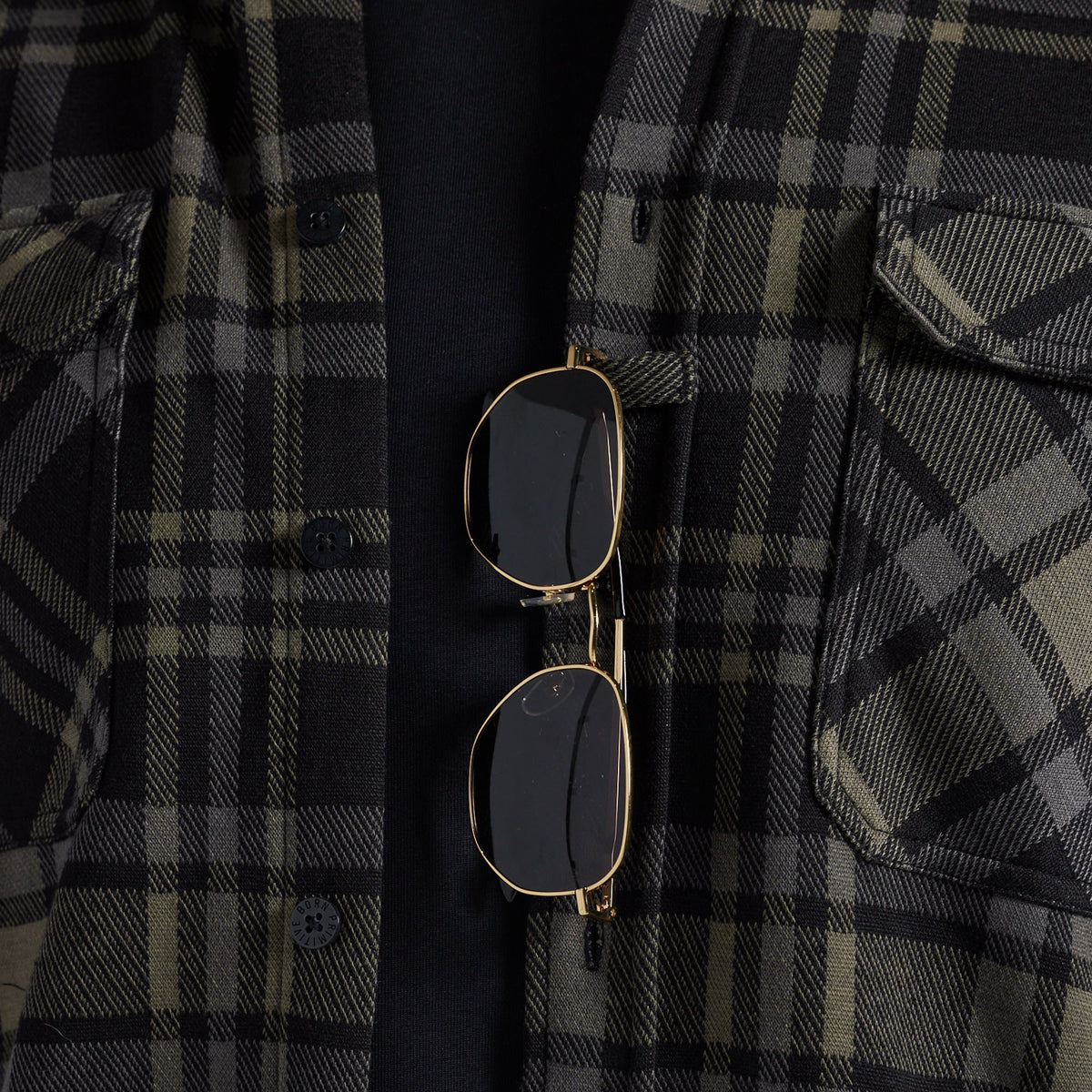 Sunglasses hanging from the placket of a black and gray plaid flannel shirt.