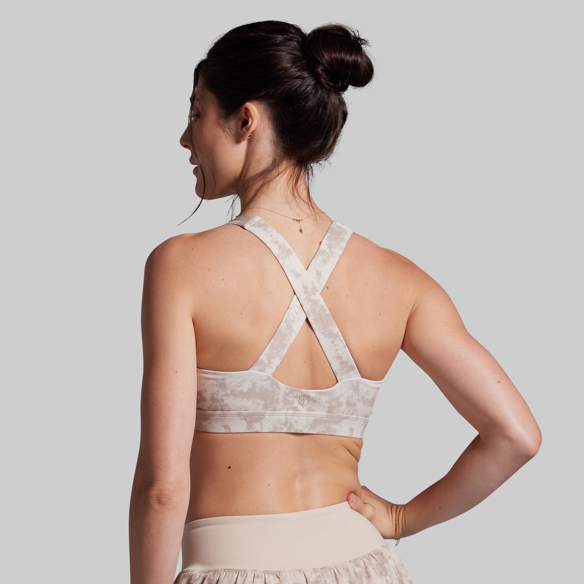 Woman wearing a light-colored sports bra and shorts on a plain background