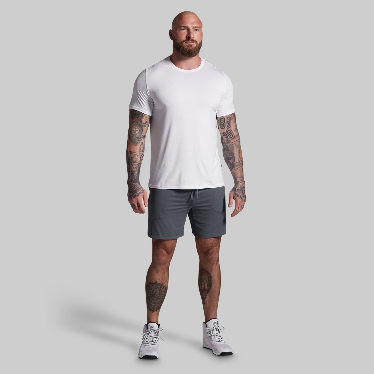 Man wearing a white t-shirt and gray shorts on a plain background