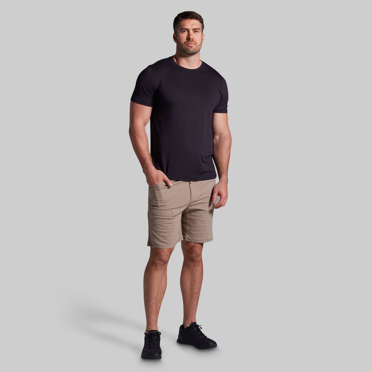 Man wearing a black t-shirt and beige shorts on a gray background