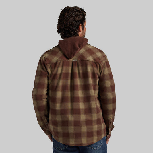 A man viewed from behind wearing a brown and tan plaid hooded flannel shirt jacket, paired with blue jeans, against a solid gray background.
