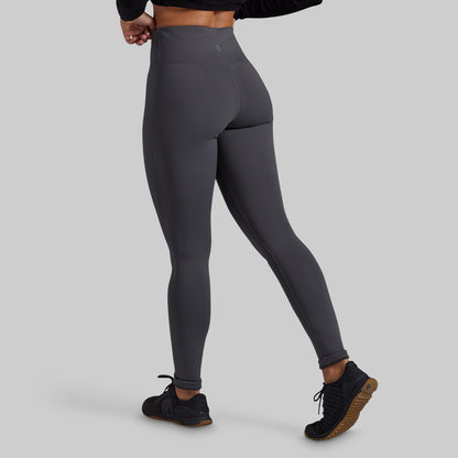 A model wearing dark gray high-waisted leggings, shown from a rear three-quarter angle against a solid light gray background.