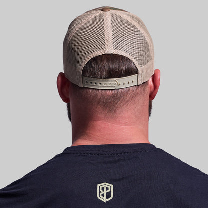 Person wearing a beige mesh cap and navy shirt with a logo on a gray background