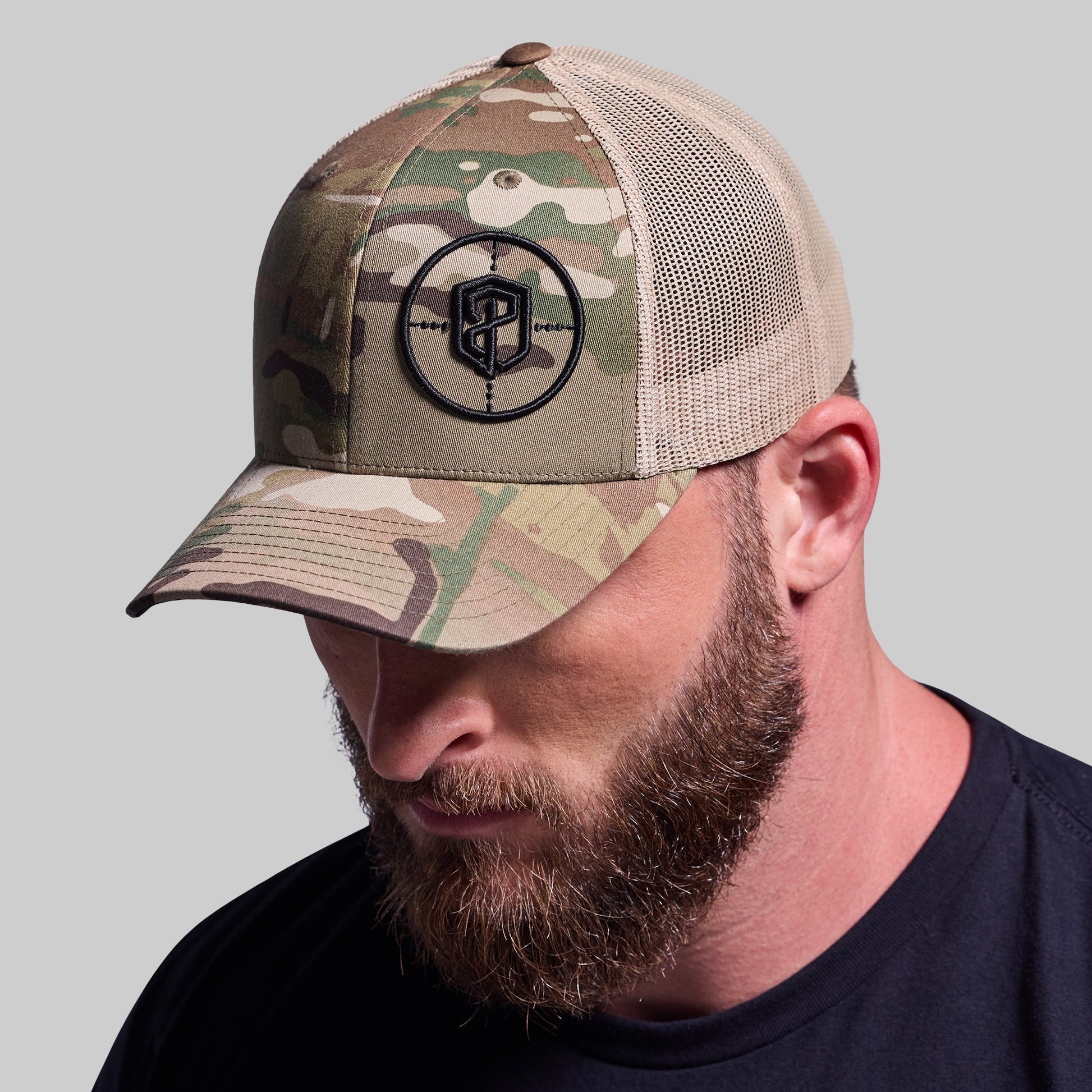 Man wearing a camouflage baseball cap with a logo on a gray background