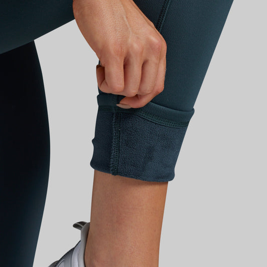 Close-up of a person's hands and lower leg pulling up the cuff of green leggings to reveal a soft, fleece-lined interior.