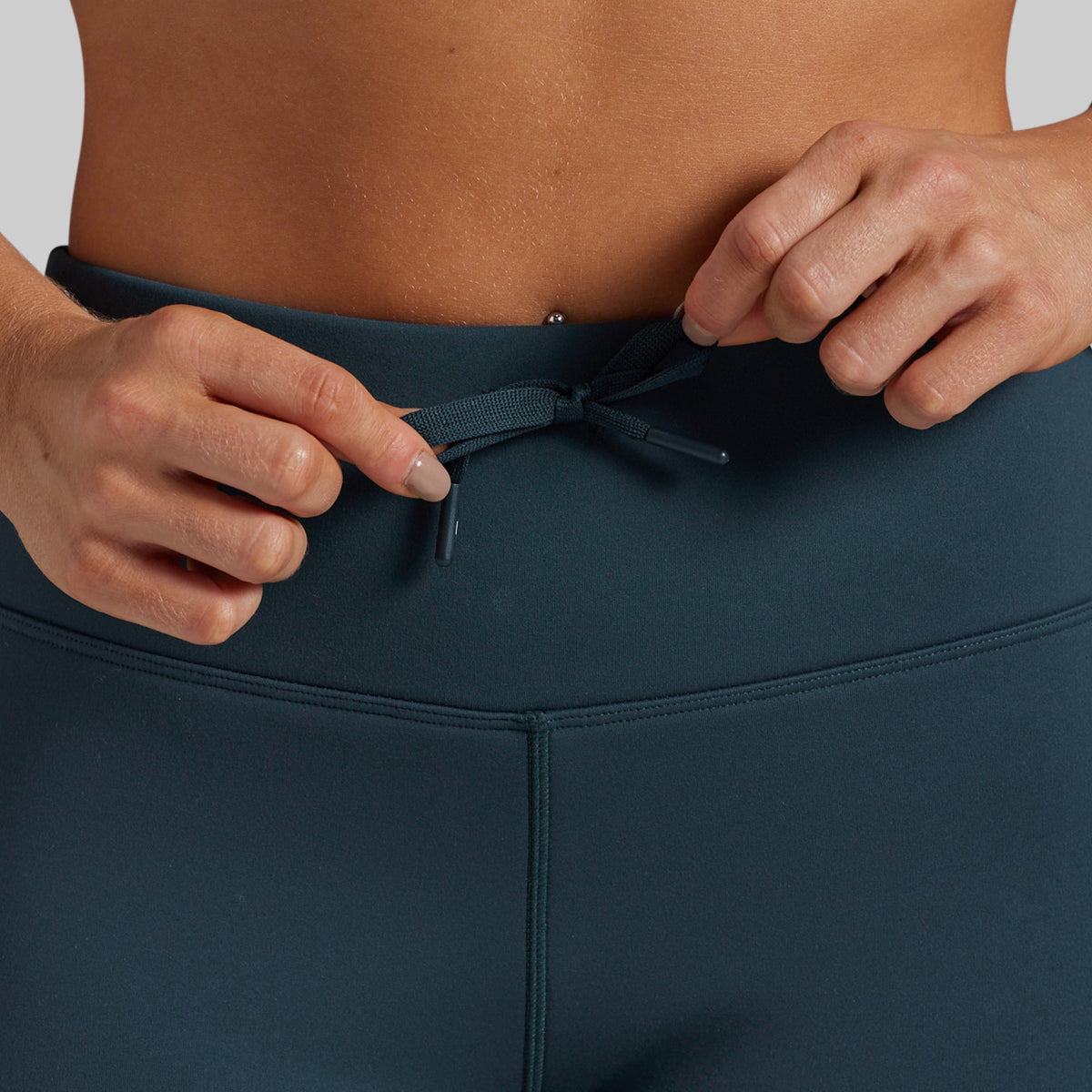 Close-up of a person wearing dark teal athletic leggings, adjusting the drawstring at the waistband.