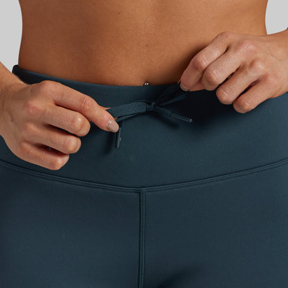 Close-up of a person wearing dark teal athletic leggings, adjusting the drawstring at the waistband.