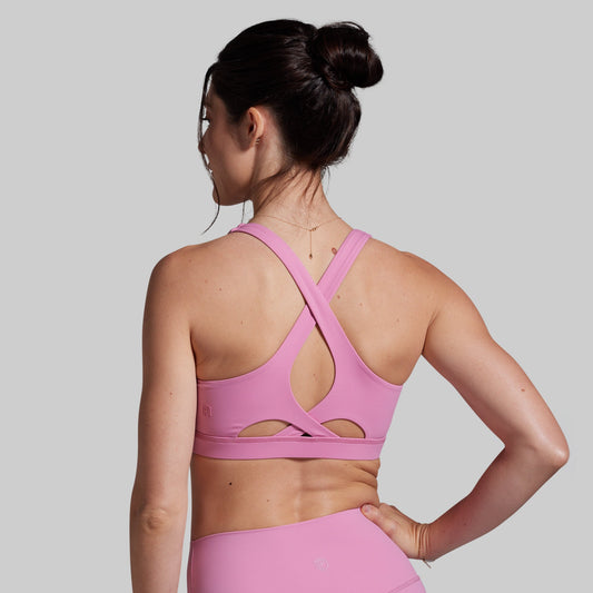 Woman wearing a pink sports bra and leggings on a gray background