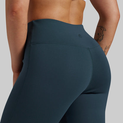 Close-up back view of a model wearing high-waisted dark teal blue-gray leggings against a light gray studio background.