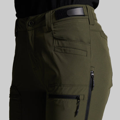 Close-up of olive green cargo pants with multiple zippered pockets and belt loops, shown on a model against a light gray background.