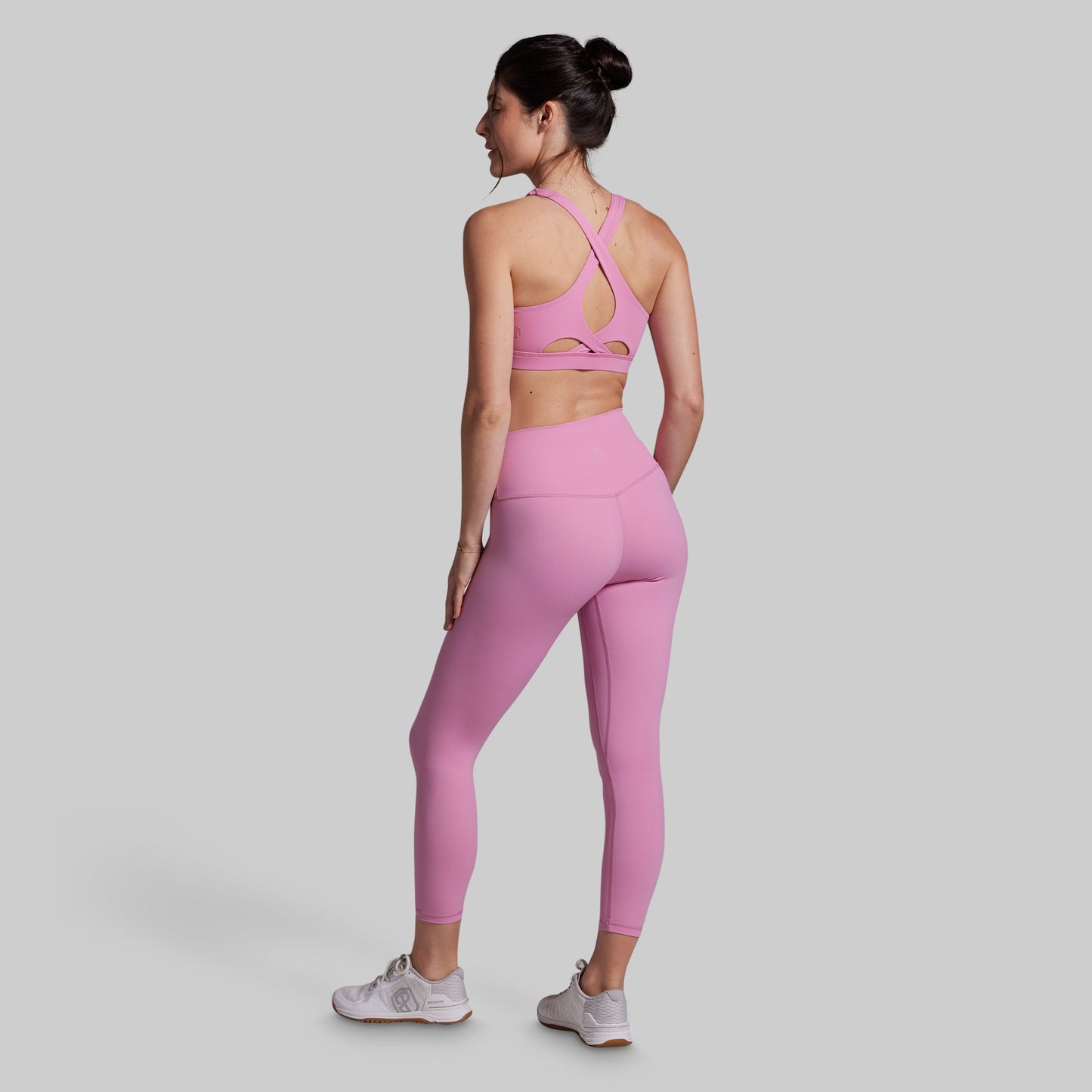Woman wearing a pink sports bra and leggings set on a gray background
