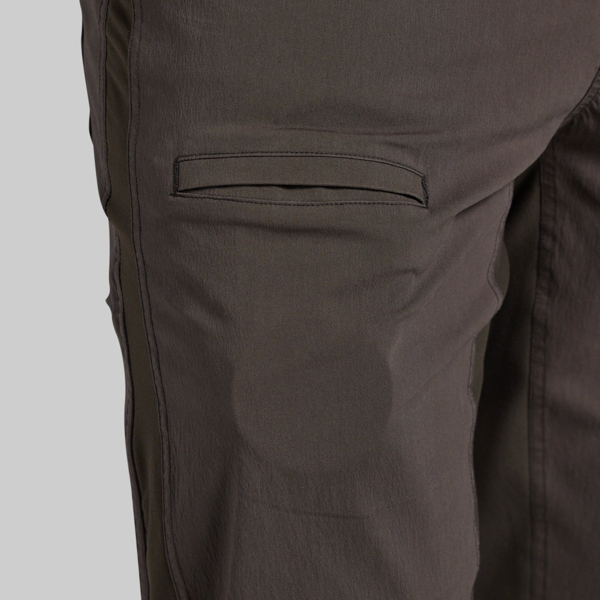 Close-up of dark brown pants showing a side pocket and fabric texture against a light gray background.