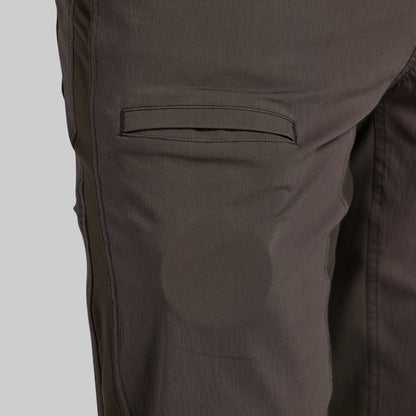 Close-up of dark brown pants showing a side pocket and fabric texture against a light gray background.