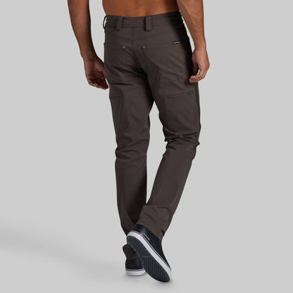 A man wearing dark brown slim-fit cargo pants, shown from the back and side against a solid light gray background.
