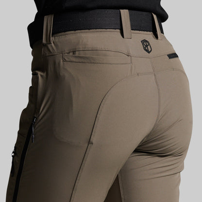 Close-up back view of a person wearing storm grey outdoor pants with a black belt, showing the rear pockets and a small shield logo near the waistband.
