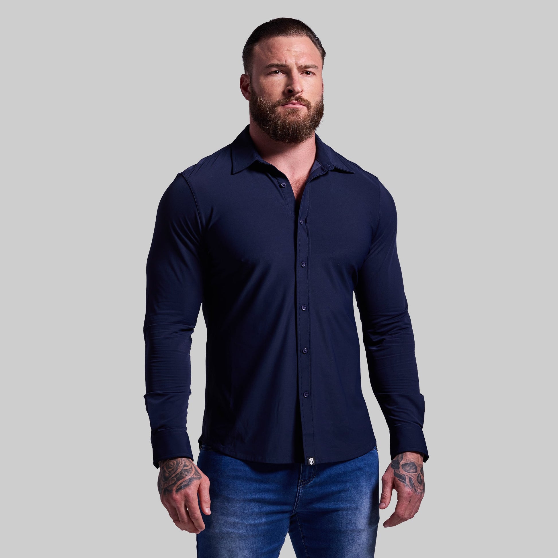 A man wearing a navy long sleeve button-down shirt and blue jeans.