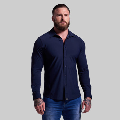 A man wearing a navy long sleeve button-down shirt and blue jeans.