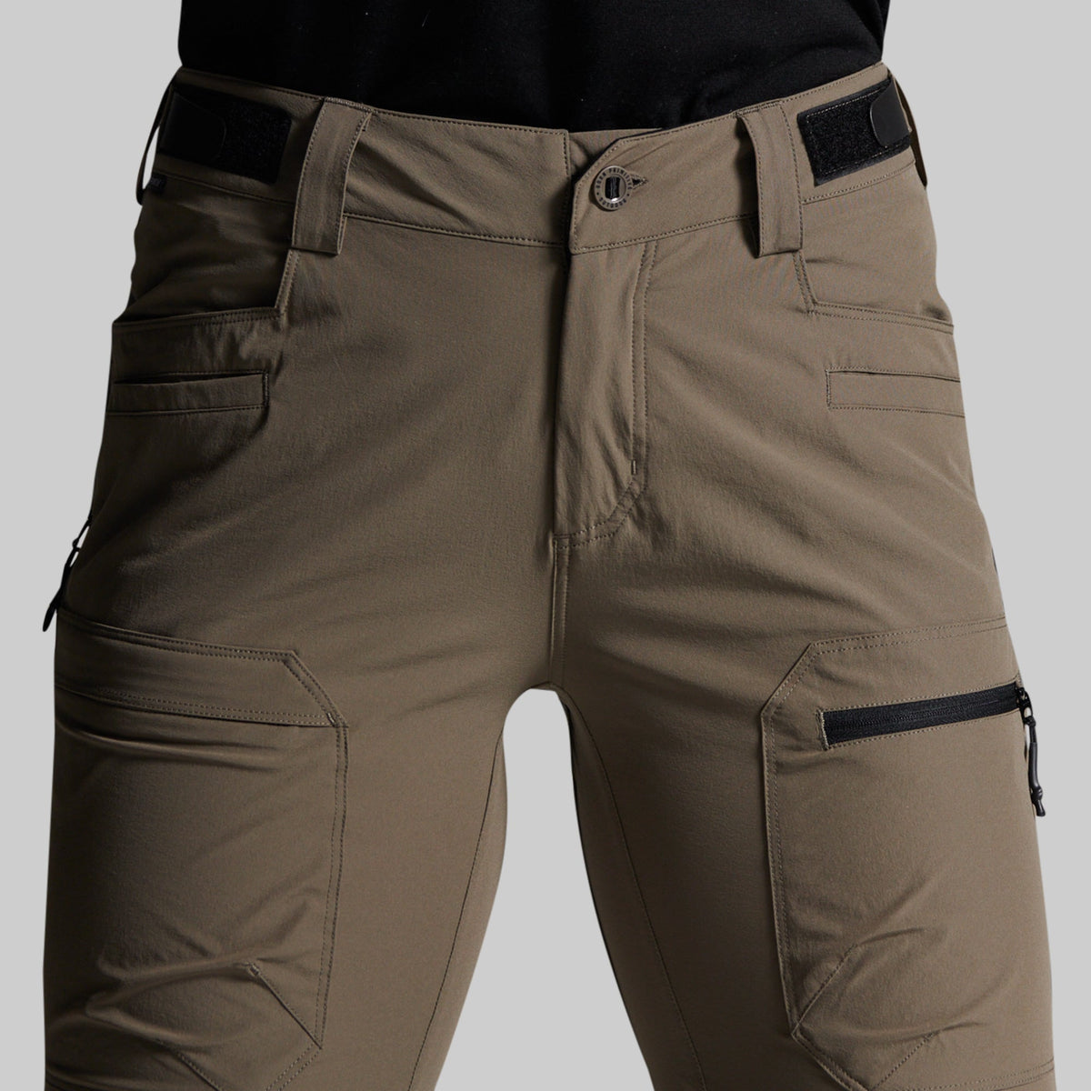 Close-up of a person wearing cargo-style pants in a storm grey color, with black belt and zipper accents, against a light gray studio background.