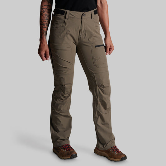 A person wearing storm grey cargo pants with a black belt, black top, and brown hiking boots, shown from the waist down against a light gray studio background.