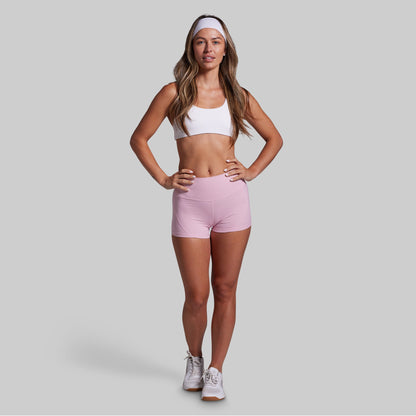 Woman wearing a white sports bra and pink shorts on a gray background