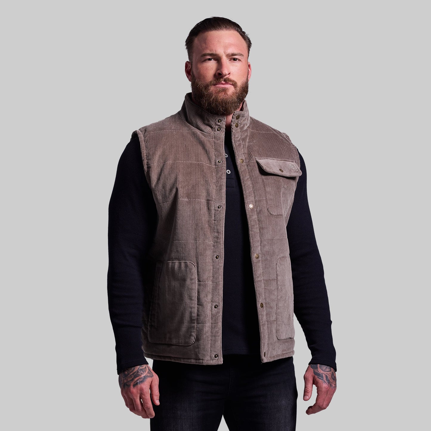 Man wearing a brown vest over a black long-sleeve shirt on a gray background