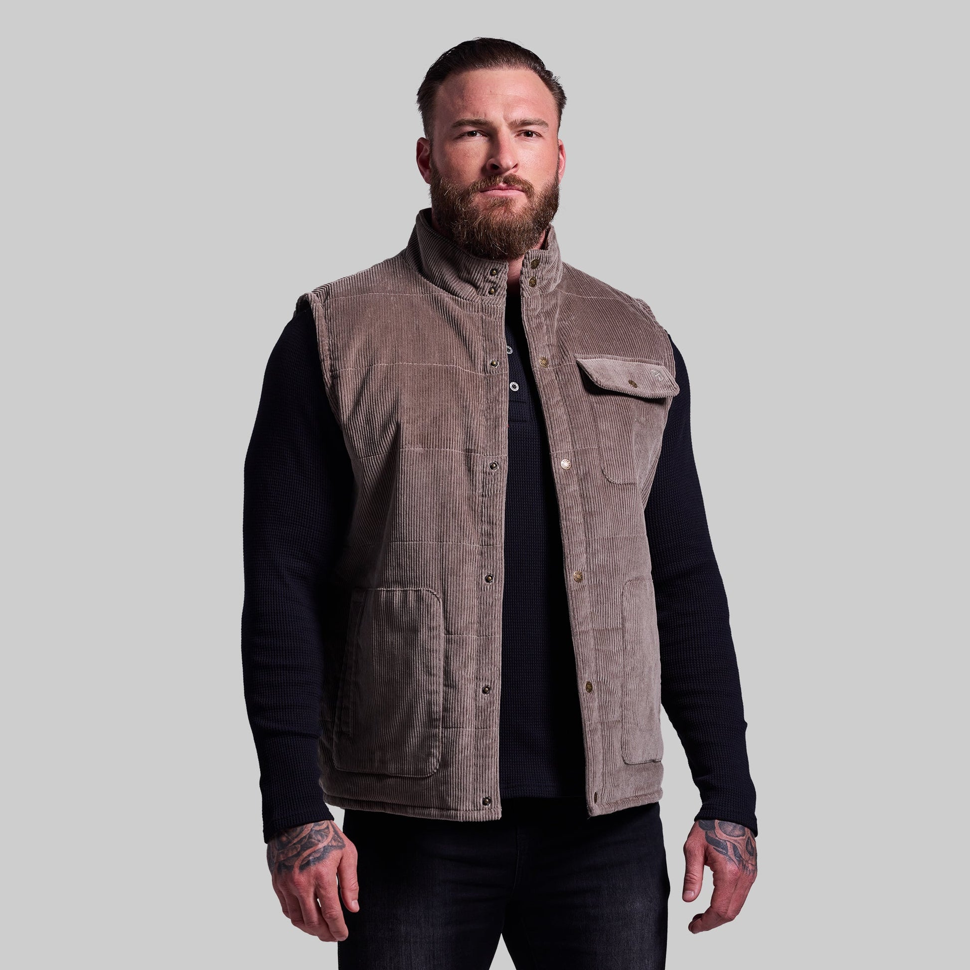 Man wearing a brown vest over a black long-sleeve shirt on a gray background