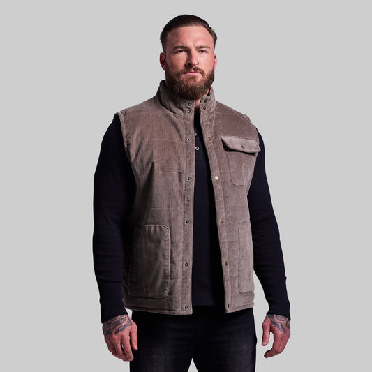 Man wearing a brown vest over a black long-sleeve shirt on a gray background