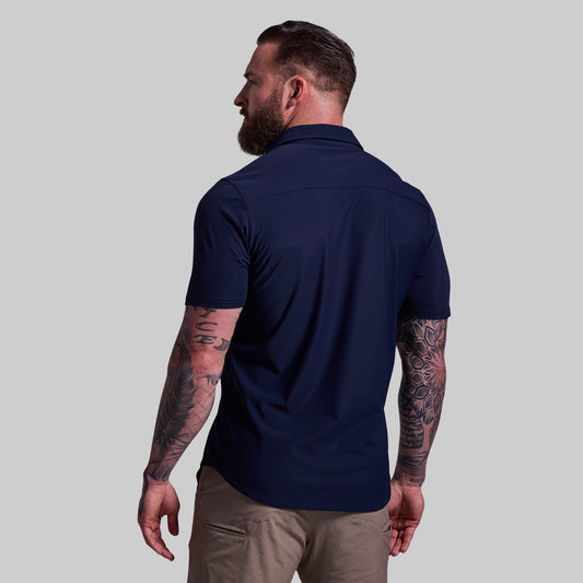 Man wearing a navy blue shirt and beige pants against a gray background