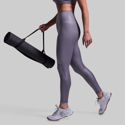 Person wearing gray leggings holding a black yoga mat on a light gray background