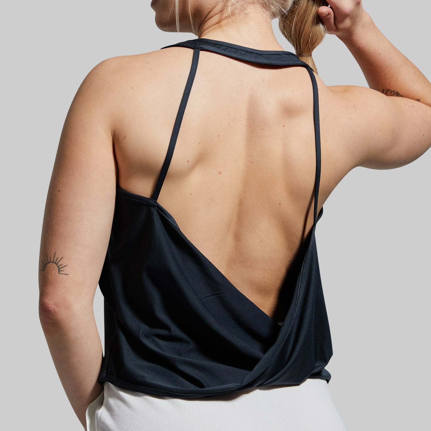 Person wearing a black open-back tank top on a plain background