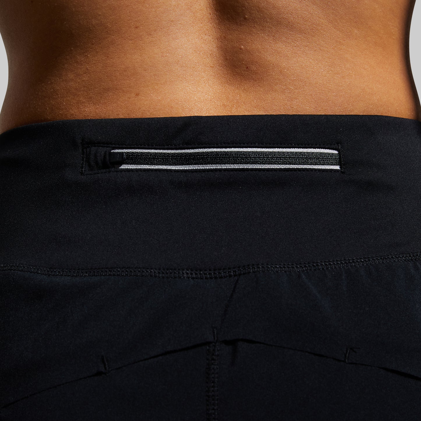 Close-up of black athletic shorts with a reflective tape on pocket zipper on a neutral background