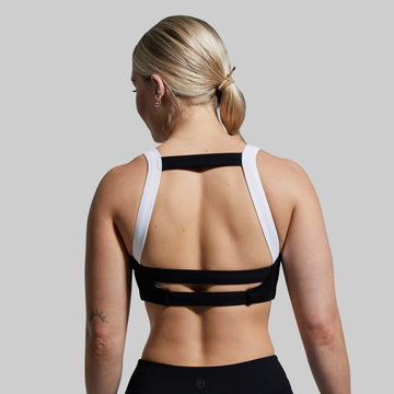Person wearing a black sports bra with white straps on a plain background