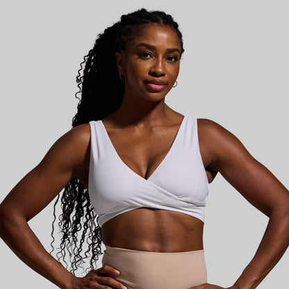Woman wearing a white sports bra and beige pants against a gray background