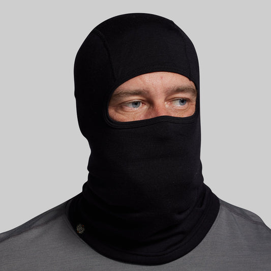 Person wearing a black balaclava against a gray background