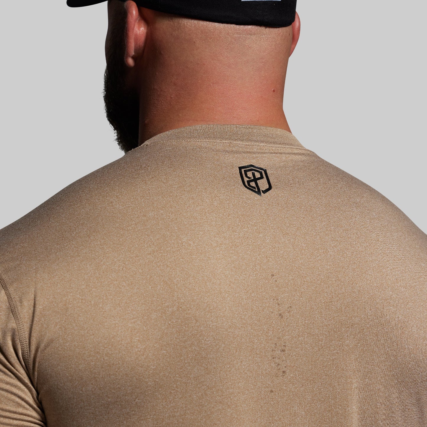 Person wearing a beige shirt with a logo on the back against a gray background